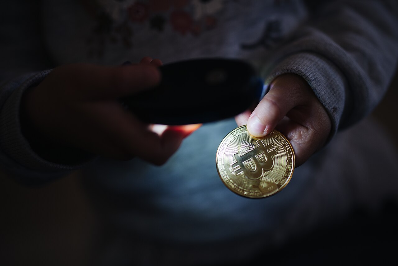 Una mano sostiene una moneda conmemorativa de bitcoin ante un fondo oscuro.