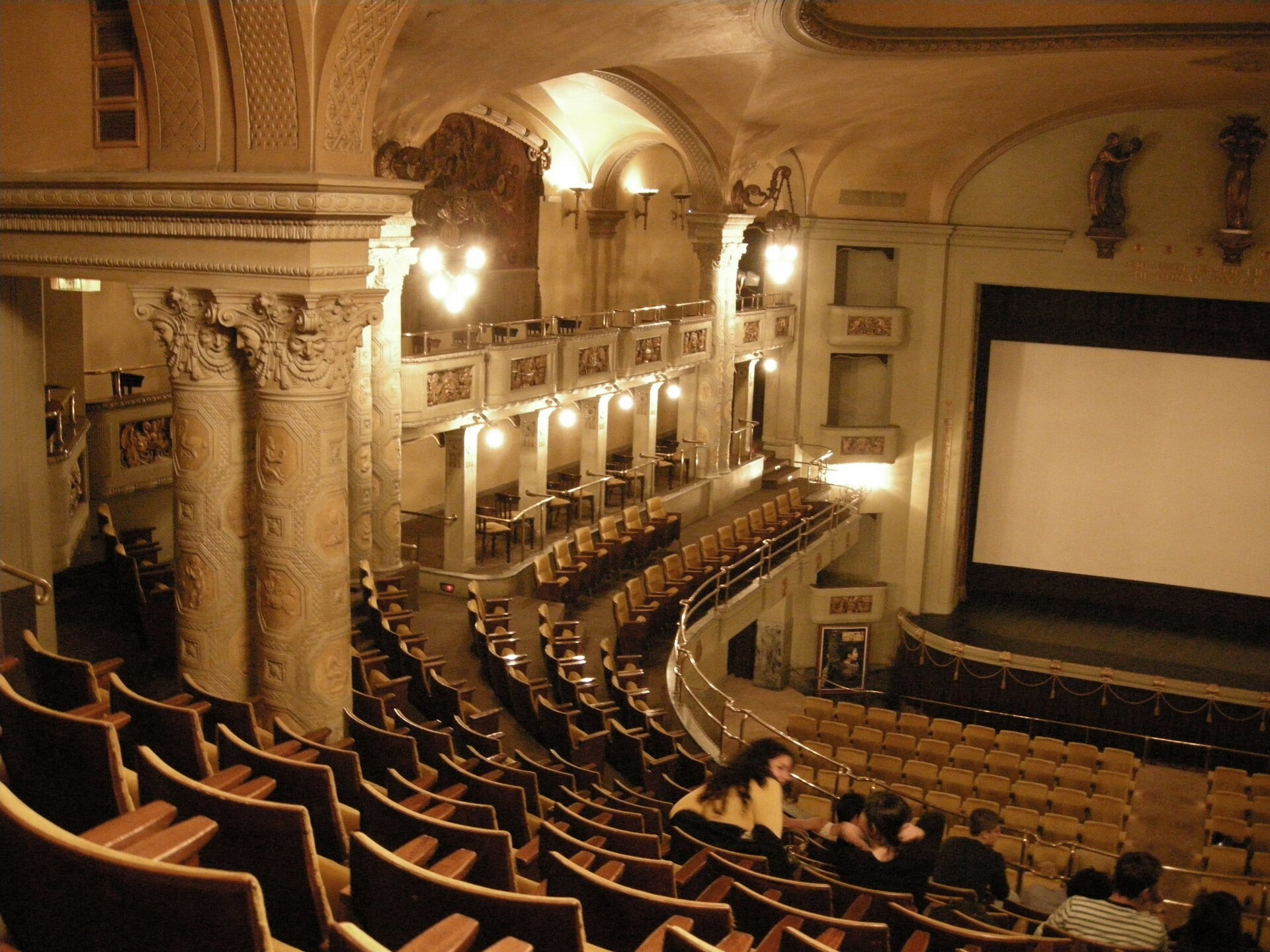 Sala de cine histórica vista desde el anfiteatro: butacas en curva, columnas decoradas y la pantalla al fondo.